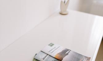 A white table with three folded brochures and a small flower lamp. In the background, there is a light curtain.