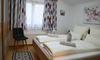 A cozy bedroom with two beds and well-maintained bedding. A chair is positioned next to a window with curtains.