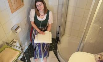 A woman is sitting on a towel in a bathroom. She is wearing a traditional dress and smiling kindly.