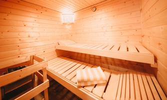 A cozy sauna with wooden paneling and two loungers. On one of the loungers lies a scattered towel.