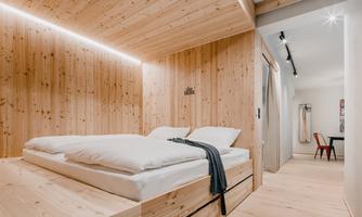 A modern room with wooden walls and a cozy bed. The space is bright and designed in a minimalist style.