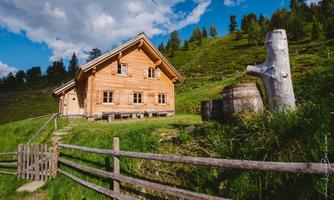A beautiful wooden house in a green mountain landscape. In the foreground, there is a wooden barrel and a tree stump.