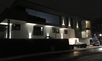 A modern building at night, illuminated by soft light. In the foreground stands a car and a Christmas tree is visible.