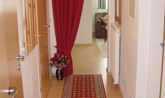 An inviting hallway with a red carpet and a curtain. At the end of the hallway, a cozy living area is visible.