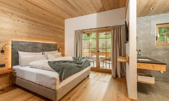 A modern bedroom with wooden walls and a large window. There is a comfortable bed and a stylish area with a sink.