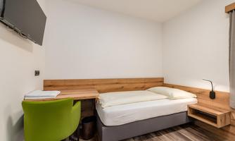 A simple room with a single bed and a desk. A television is mounted on the wall and a chair provides additional comfort.