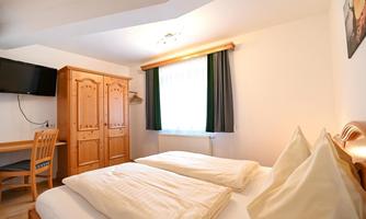 A cozy bedroom with a double bed and two pillows. The room is bright and contains a table, chairs, and a television.