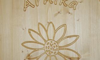 A wooden sign with the name "Arnika" and a flower illustration. The surface has a natural wood texture.