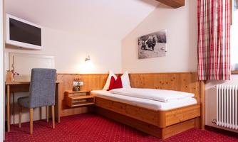 A cozy room with a single bed and a table. The walls are panelled with wood and a television is available.