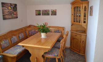 A cozy dining area with a wooden tray and benches. A plant arrangement in the center of the table and a display cabinet in the background.