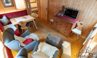 A cozy room with wooden walls and a warm ambiance. There is a dining area, comfortable armchairs, and a television.