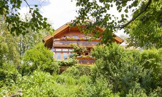 A cozy wooden house surrounded by lush greenery. The balconies are adorned with flowers, creating an inviting atmosphere.