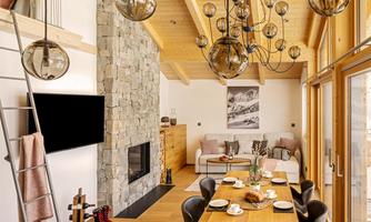 A modern living room with a stone fireplace and large windows. Plates and cups are on the table, and the lighting is stylish.