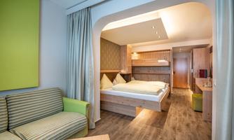 A modern hotel room with a double bed and a cozy seating area. The decor is bright and inviting with wood and green tones.