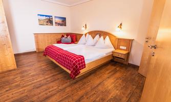 A cozy bedroom with a large double bed and decorative pillows. The walls are painted in warm tones, and the wooden flooring creates an inviting atmosphere.