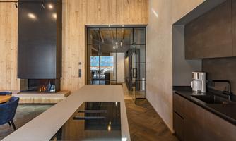 A modern kitchen with a large kitchen island and black work area. The walls are made of light wood, and a cozy fireplace creates an inviting atmosphere.