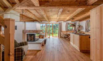 A modern, bright living space with wooden ceilings and a fireplace. Large windows offer a view of nature outside.