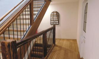 A bright hallway with a wooden staircase and a mirror on the wall. The floor is made of light wood and the walls are painted in neutral tones.