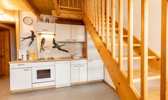 A bright kitchen with modern appliances and wooden shelves. A staircase leads to the upper floor.