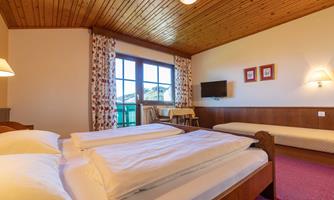 A cozy bedroom with two beds and a wooden ceiling. Large windows offer a view outside and provide plenty of daylight.