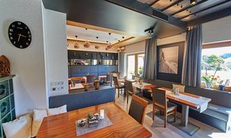 A modern restaurant with wood and stone decor. The tables are elegantly set and large windows provide a view of the outdoors.