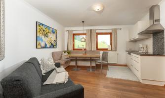 A bright and modern apartment with a cozy living area and a dining table. The windows provide a view of the beautiful nature.