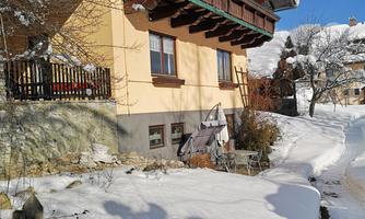 A cozy house with a balcony, surrounded by snow. The sky is clear and blue.