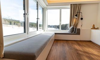 A modern room with large windows and a cozy seating area. The view extends over snow-covered landscapes and forests.