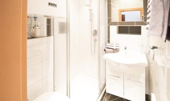 A modern bathroom with a shower and a sink. The walls are tiled in light colors and the furnishings are minimalist.