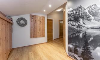 A modern hallway with wooden floors and attractive wall paneling. On one wall, there is an impressive black-and-white photo of mountains and a lake.