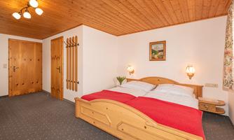 A cozy bedroom with a double bed and red blankets. The walls are made of wood, and there is a typical alpine decoration.