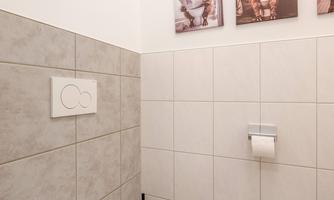 A modern toilet with gray tiles and a white toilet. Some pictures are hanging on the wall.