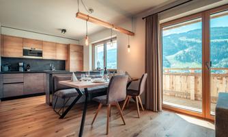 A modern kitchen with a dining table and chairs. Large windows provide a beautiful view of the mountains.