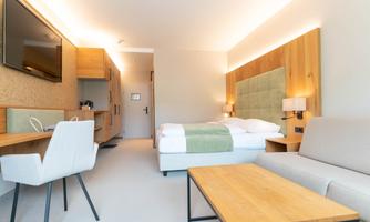 A modern hotel room with a double bed, a desk, and a seating area. The warm colors and soft lighting create an inviting atmosphere.