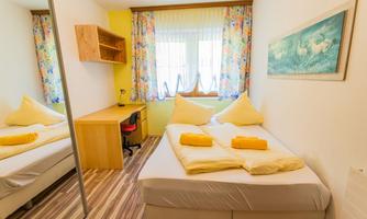 A cozy bedroom with two beds and colorful curtains. The room has a desk and is bright and inviting.