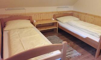 A simple bedroom with two single beds and a small table. The walls are made of wood and the floor is carpeted.