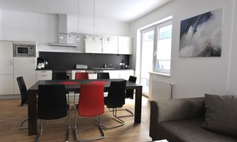 A modern kitchen with a dining area and a large table. The furniture is sleek and the colors are bright and inviting.
