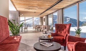 A modern living room with red armchairs and a round table. In the background, there are large windows with a view of snow-covered mountains.