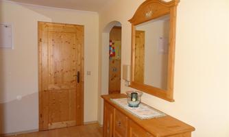 A cozy hallway with bright walls and a wooden table. A large mirror hangs on the wall and a wooden dresser stands in front of the door.