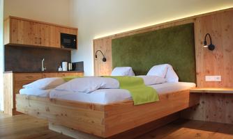 A modern room with a double bed and wooden paneling. The atmosphere is bright and inviting, with a green accent wall.