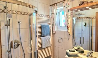 A modern bathroom with a shower and a sink. Towels in various colors are neatly arranged.