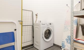 A clean laundry room with a washing machine and a clothes dryer. There are shelves on the wall with various utensils.