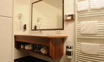 A modern bathroom with a wooden washstand and a large mirror. Towels are neatly placed on a towel rack.
