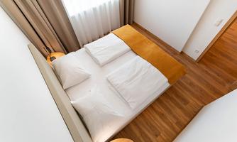 A modern bedroom with a large bed and bright curtains. The floor is made of wood and the decor is minimalist.