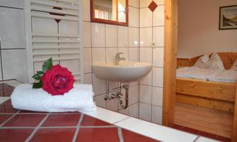 A cozy bathroom with a white towel and a red rose. In the background, a bed and a window are visible.