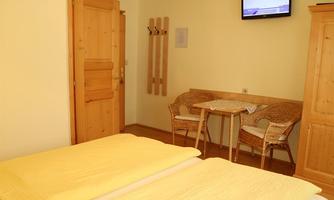 A cozy room with two beds and yellow blankets. There is a table with chairs and a television on the wall.