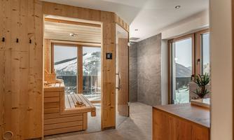 A modern wellness area with a wooden sauna and large windows offering a view of the snow-capped mountains. The atmosphere is relaxed and inviting.