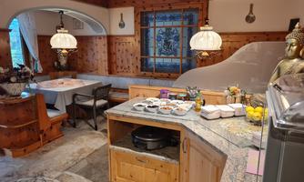 A cozy kitchen with a wooden table, a Buddha statue, and many ingredients on the countertop. The warm lighting and wooden design create an inviting atmosphere.