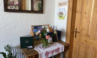 An inviting entrance area with a wooden table, on it a flower vase with colorful flowers. Mirrors and pictures hang on the wall, and a wooden door leads outside.