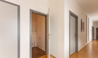 A bright hallway with several doors. One door leads to a bathroom, while the other rooms are visible in the background.